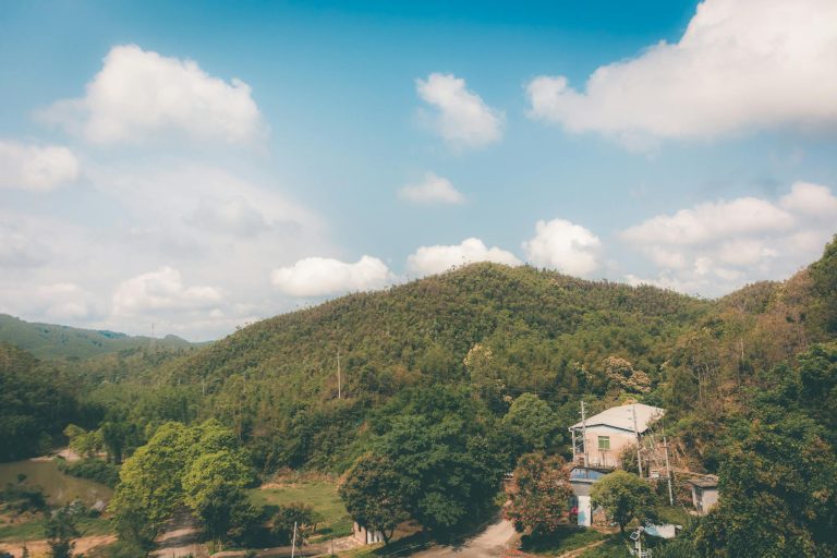 Scenic view of a rural Chinese landscape with a house, hills, and lush greenery under a bright blue sky.